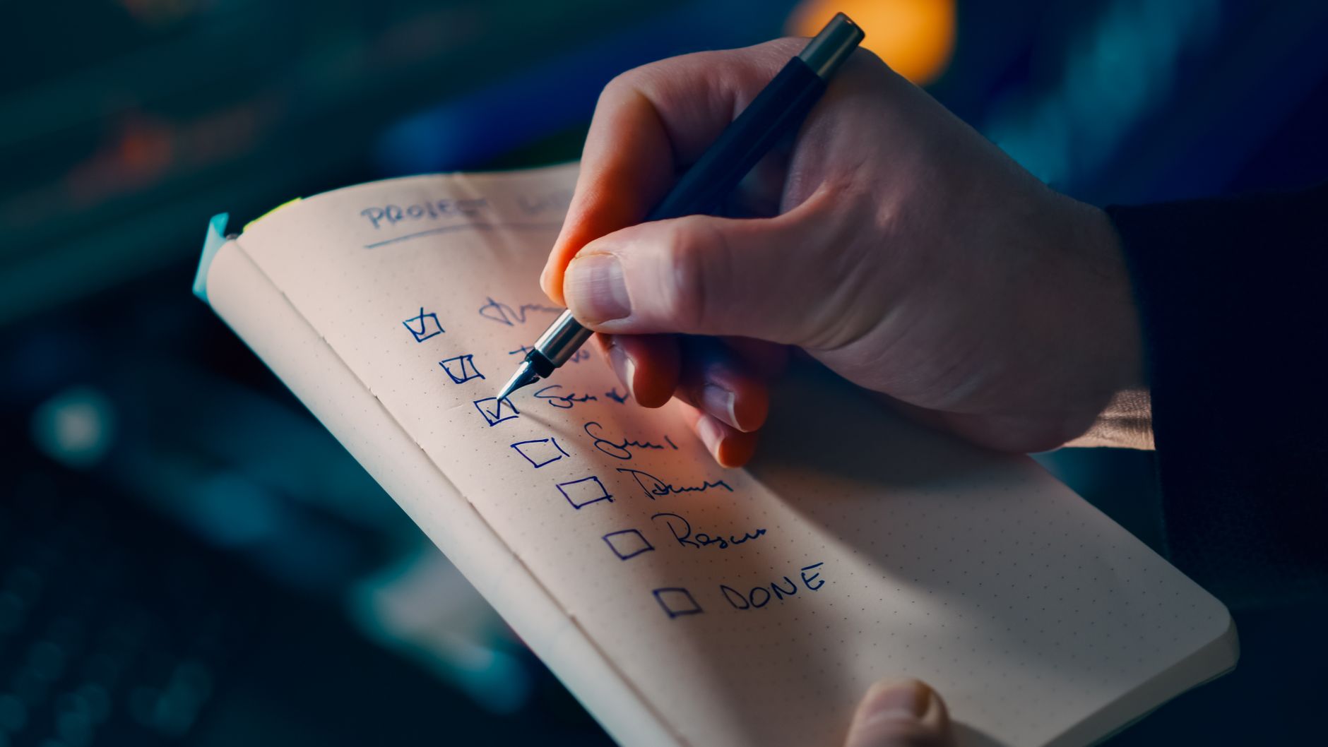 Dłoń zapisuje checklistę w notesie podczas planowania badań online