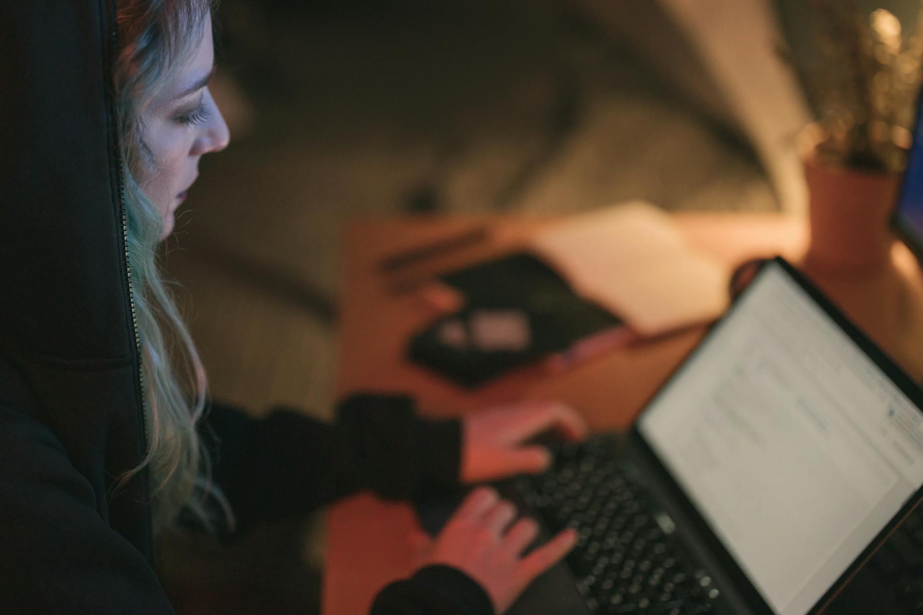 Młoda kobieta pracuje przy laptopie przy przyciemnionym biurku