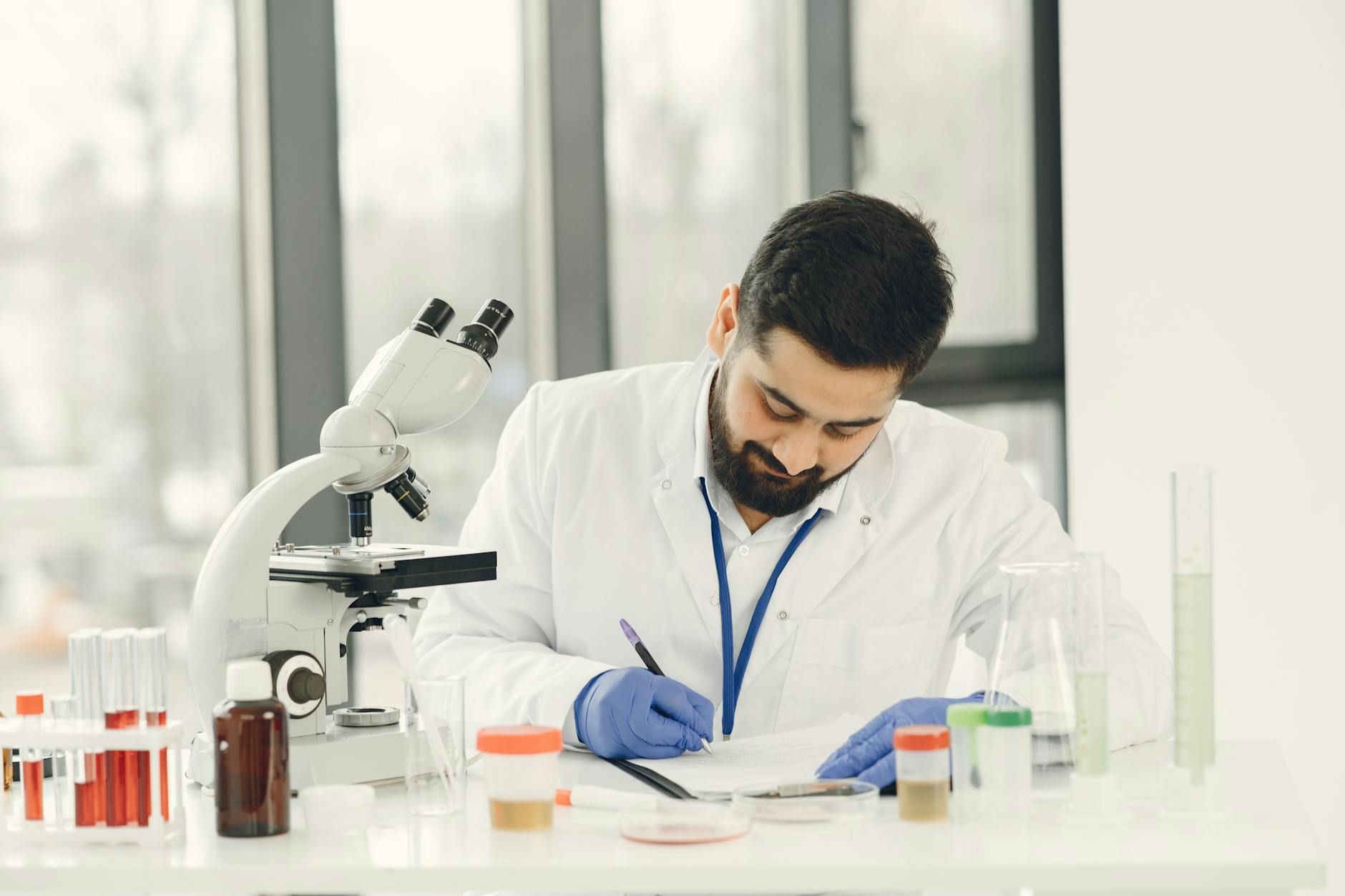 Naukowiec robi notatki przy mikroskopie i szklanym sprzęcie laboratoryjnym