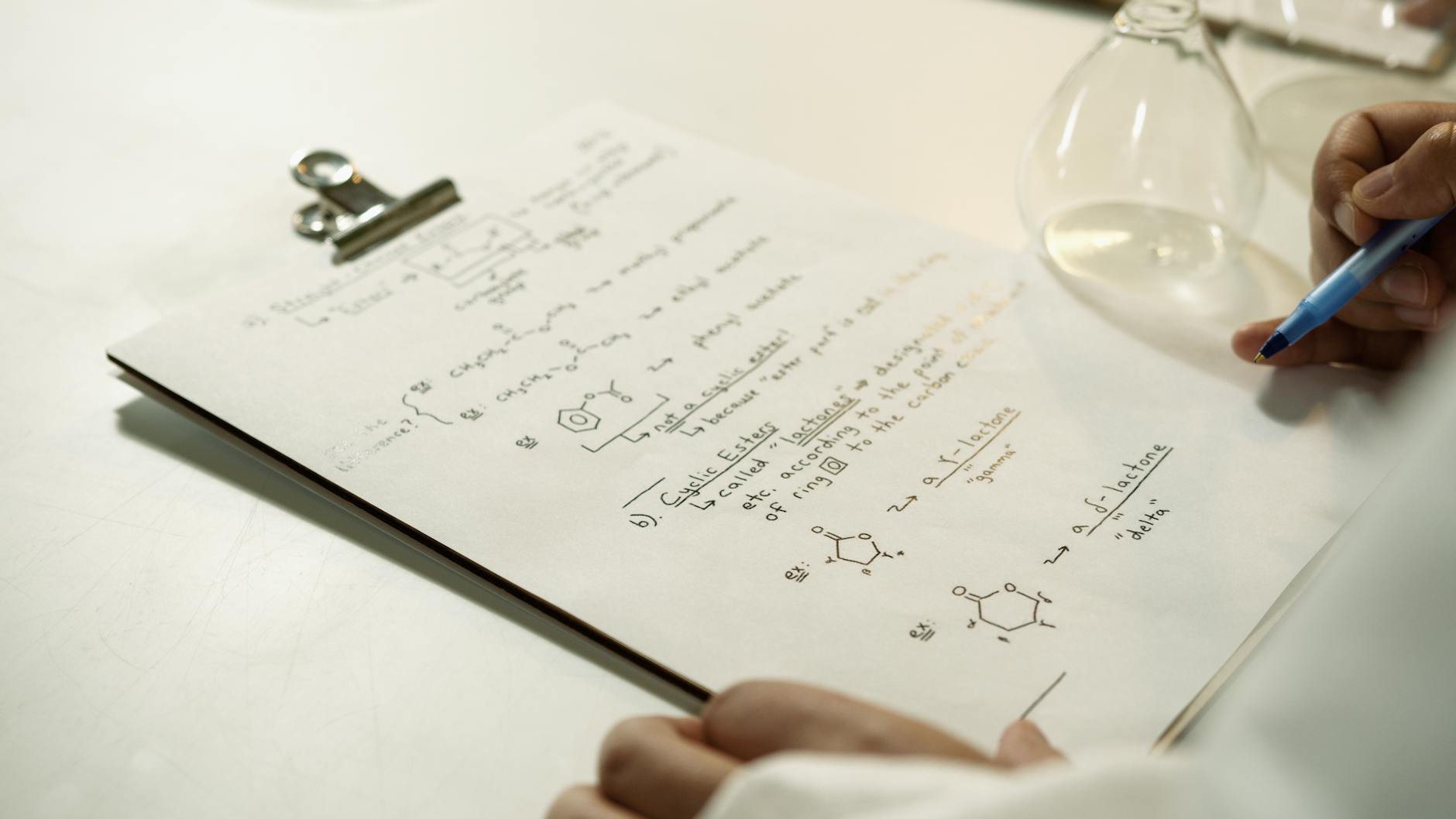 Zbliżenie na odręczne wzory chemiczne na klipbordzie w laboratorium