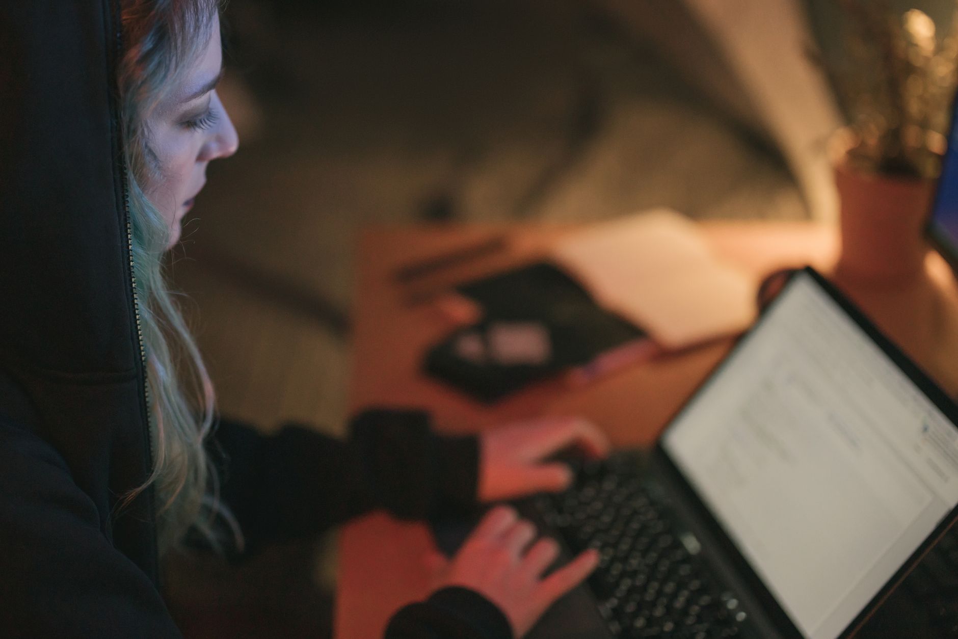 Kobieta pracująca przy laptopie nocą w przyciemnionym, przytulnym pokoju